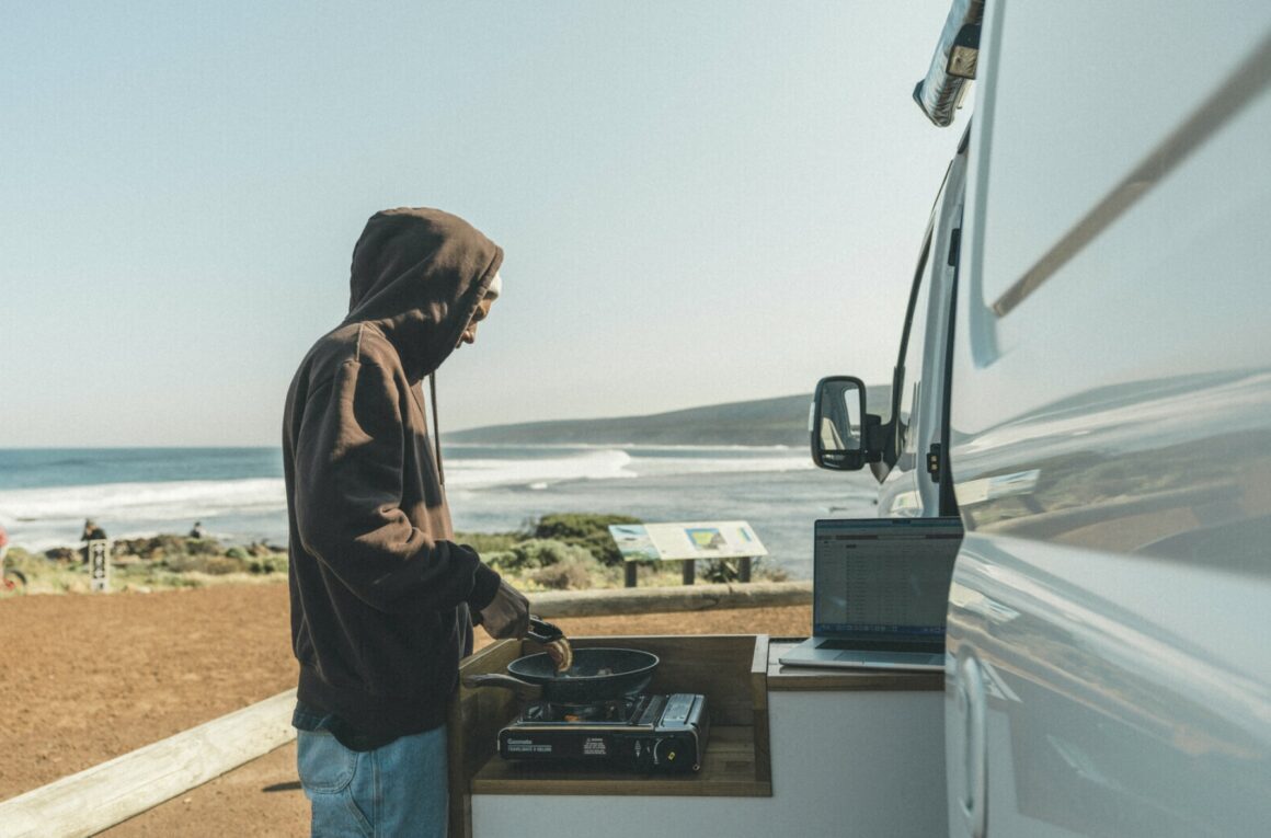A man cooks dinner out of his OnlyVans campervan on the beach front. This is one of the best campervans to hire in Western Australia (WA).